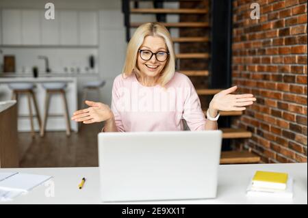 Une femme d'âge moyen surprise regarde l'écran de l'ordinateur portable avec un rire et un malentendu, une femme de milieu d'âge ne comprend pas ce qui s'est passé et les haussles Banque D'Images