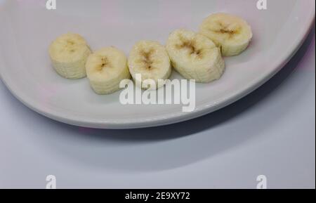 Cinq tranches de banane disposées sur une assiette blanche sur fond blanc Banque D'Images