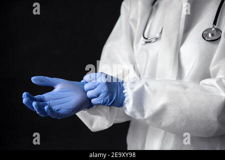 Médecin en combinaison médicale PPE avec stéthoscope, gros plan des mains. Le médecin met des gants de protection à l'hôpital. Concept de soins professionnels, diagnostic a Banque D'Images