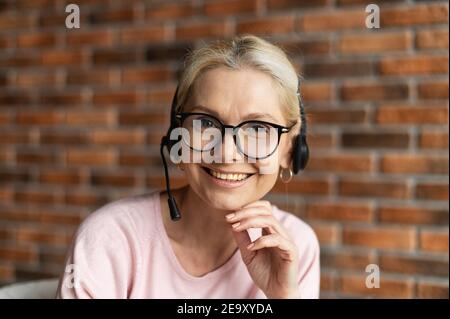 Une femme d'âge moyen, serviable et sympathique, qui porte un casque et des yeux stylés regarde l'appareil photo et sourit. Gros plan sur l'appel d'une femme de milieu d'âge Banque D'Images