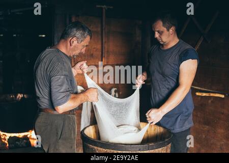Carpathian Mountains, Ukraine - août 2020 : deux hommes qui font du fromage de ferme. Drainer le lactosérum par le cheesecloth. Banque D'Images