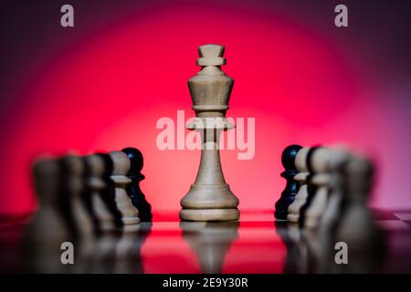 Chess White King sur chessboard avec un fond de dégradé rouge Entouré de pions blancs et noirs - mise au point unique le roi Banque D'Images