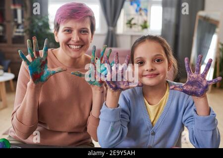 Portrait de la femme et de la petite fille montrant leurs mains peintes et sourire à l'appareil photo tout en peignant ensemble Banque D'Images