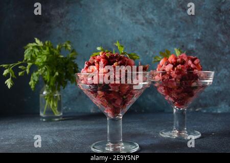 Vinegret ou vinaigrette. Salade rouge russe traditionnelle avec légumes cuits et marinés, petits pois, betteraves, dans deux bols en verre sur fond gris. Banque D'Images