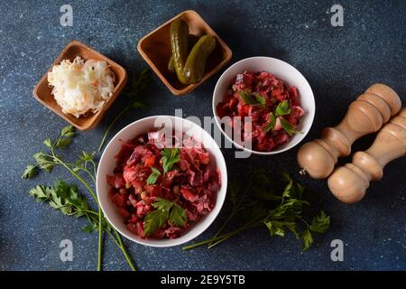 Vinegret ou vinaigrette. Salade rouge russe traditionnelle avec légumes cuits et marinés, petits pois, betteraves, dans un bol blanc sur fond gris. Banque D'Images