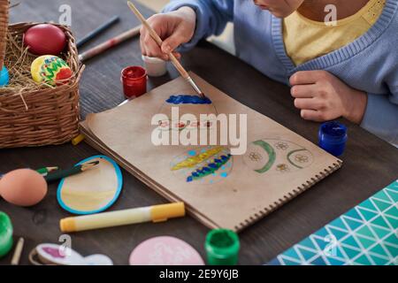 Gros plan d'un enfant assis à la table et peignant des œufs Sur papier pour les vacances de Pâques Banque D'Images