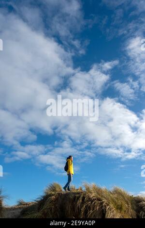 Randonnée de randonneurs femelles le long de hautes dunes de sable. Veste jaune et sac à dos contre un ciel bleu. Banque D'Images