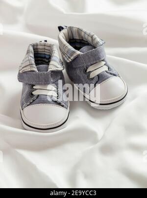 Baptême de baptême, baptême de bébé. Chaussons bébé garçon sur fond blanc satiné. Chaussures douces pour bébé, nouveau-né, invitation, cérémonie, chaussures en soie Banque D'Images