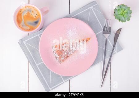 Vue rapprochée en haut d'un morceau de tarte sur une assiette rose avec un couteau et une fourchette sur une serviette en lin pliée avec un motif géométrique et une tasse avec café. H Banque D'Images