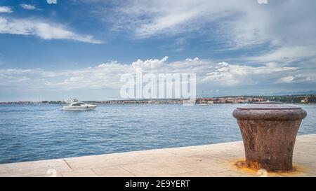 Bateau à moteur naviguant dans la baie de Zadar et simple, vieux et rouillé bollard de mouillage sur la jetée. Mer Adriatique et côte de la ville de Zadar, Croatie Banque D'Images