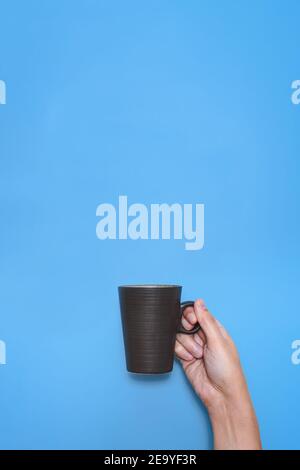 prise verticale de la main d'un homme caucasien méconnaissable tenant une tasse marron foncé avec un fond bleu Banque D'Images