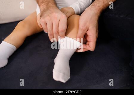 Le jeune père met des chaussettes sur son fils, assis sur un canapé Banque D'Images