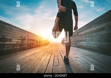 Homme chauffant et étirant les jambes avant de courir à l'extérieur au coucher du soleil ou lever du soleil Banque D'Images