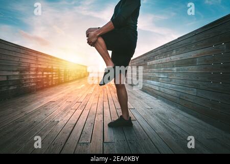 Homme se réchauffant et étirant les jambes avant de s'entraîner à l'extérieur à coucher ou lever du soleil Banque D'Images