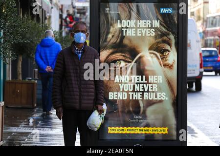 Londres, Royaume-Uni. 02 février 2021. Un homme portant un masque facial se trouve à côté de l'affiche de campagne publicitaire du NHS Covid-19 à Londres. Le gouvernement britannique a déclaré qu'il vaccine plus de 50 ans d'ici mai 2021. Crédit : SOPA Images Limited/Alamy Live News Banque D'Images