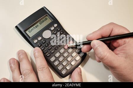 Un homme qui calcule sur une calculatrice scientifique noire avec une erreur sntax texte à l'écran Banque D'Images