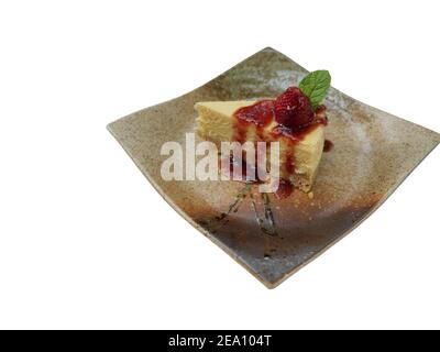 Tranche de tarte au cheesecake recouverte de sirop de fraise et de feuilles de menthe sur une plaque en céramique carrée, nourriture sucrée isolée sur fond blanc Banque D'Images