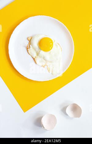 Œuf frit sur une assiette blanche, sur fond jaune et blanc. Composition créative minimale avec espace de copie, vue du dessus. Banque D'Images