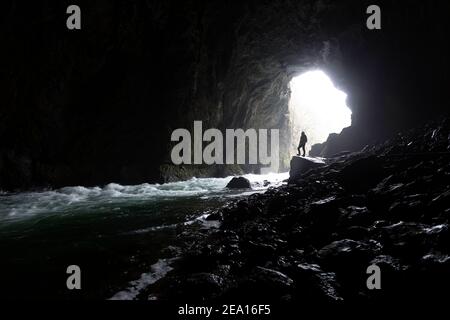 Femme avec un phare debout sur le rocher au bord de la rivière à l'entrée de la grotte de Tkalca dans le parc de Rakov Skocjan, Slovénie Banque D'Images