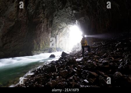 Femme avec un phare debout sur le rocher au bord de la rivière à l'entrée de la grotte de Tkalca dans le parc de Rakov Skocjan, Slovénie Banque D'Images