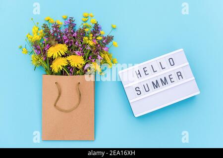 Texte Hello Summer on light box et bouquet lumineux de fleurs sauvages en paquet artisanal sur fond bleu. Concept heure d'été. Vue de dessus modèle de Flat Lay Banque D'Images
