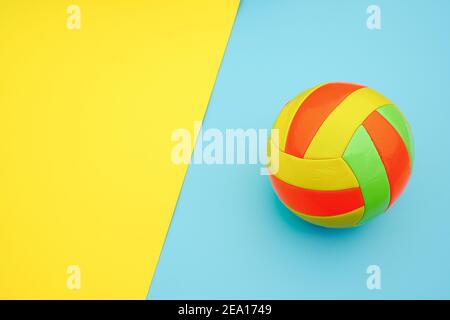 Boule de volley multicolore lumineuse sur fond bleu jaune avec espace de copie. Vue de dessus Flat Lay style minimal modèle pour carte, conception. Banque D'Images