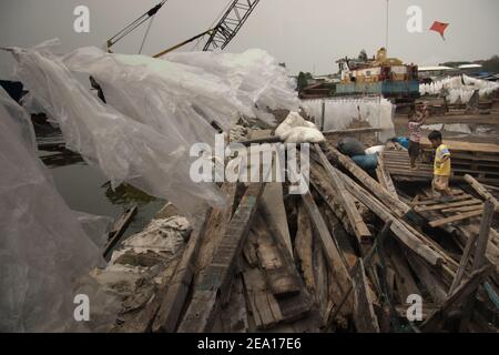 Enfants jouant du cerf-volant à proximité de matériaux en bois, structure de protection côtière, couvertures en plastique séchées au soleil et machinerie lourde sur la côte de Jakarta, Indonésie. Banque D'Images