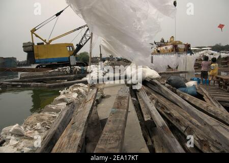 Enfants jouant du cerf-volant à proximité de matériaux en bois, structure de protection côtière, couvertures en plastique séchées au soleil et machinerie lourde sur la côte de Jakarta, Indonésie. Banque D'Images
