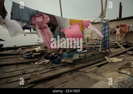 Une femme séchant une buanderie au soleil, sur la terrasse en bois de sa maison dans la zone côtière de Jakarta, Indonésie. Plusieurs maisons de la région ont été construites au-dessus de l'eau de mer sur pilotis, juste à l'extérieur de la structure de protection côtière reliant la communauté avec une route côtière et leurs voisins terrestres. Muara Baru, Penjaringan, Nord de Jakarta, Jakarta, Indonésie. Photo d'archive. Banque D'Images