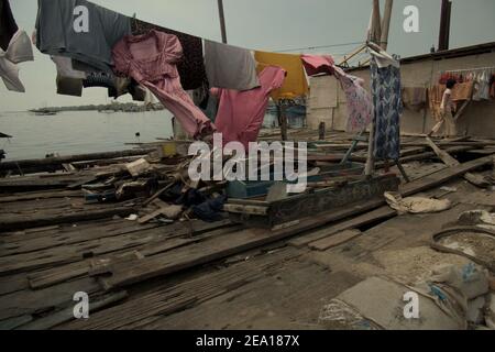 Une femme séchant une buanderie au soleil, sur la terrasse en bois de sa maison dans la zone côtière de Jakarta, Indonésie. Plusieurs maisons de la région ont été construites au-dessus de l'eau de mer sur pilotis, juste à l'extérieur de la structure de protection côtière reliant la communauté avec une route côtière et leurs voisins terrestres. Muara Baru, Penjaringan, Nord de Jakarta, Jakarta, Indonésie. Photo d'archive. Banque D'Images