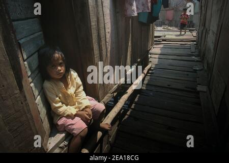 Un enfant assis sur la porte d'une maison dans la région de Muara Baru, dans la zone côtière de Jakarta, en Indonésie. Plusieurs maisons de la région ont été construites au-dessus de l'eau de mer sur pilotis, juste à l'extérieur de la structure de protection côtière reliant la communauté avec une route côtière et leurs voisins terrestres. Muara Baru, Penjaringan, Nord de Jakarta, Jakarta, Indonésie. Photo d'archive. Banque D'Images