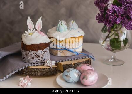 Gâteaux de Pâques en bois décorés avec des oreilles de lapin, œufs sur le plateau au premier plan, lilas sur le fond. - pain de Pâques traditionnel Kulich, paska. T Banque D'Images