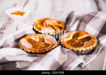 Tartelettes arrosées de sucre en poudre avec confiture de pêche sur fond de bois blanc et serviette de cuisine. Décoration de Pâques. Mise au point sélective Banque D'Images