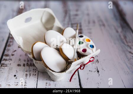 Biscuits de Pâques oeufs avec coloration alimentaire dans un oeuf de papier support sur fond en bois blanc Banque D'Images