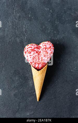 Beignet en forme de coeur dans un cône de gaufre de glace sur fond noir. Cuisine créative pour St. Saint Valentin. Banque D'Images