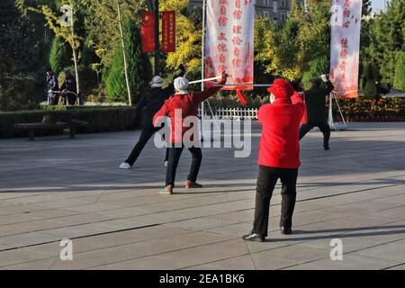 Groupe de praticiens taijian-sabre tai chi au soleil du matin réalisez des chorégraphies d'escrime au son de la musique portable comme si l'entretien doit être effectué Banque D'Images