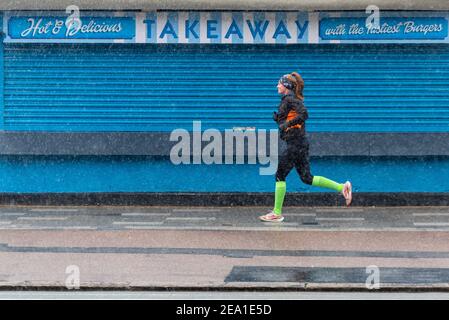 Southend on Sea, Essex, Royaume-Uni. 7 février 2021. La tempête Darcy a atteint Southend on Sea plus tard que prévu, la zone restant humide pendant la nuit. De la neige et des averses de neige sont arrivées vers 7h du matin, ce qui n'a pas dissuadé les joggeurs. Les avertissements de verrouillage COVID 19 restent en place. Femme coureur de vêtements pour temps froid passant devant une entreprise fermée en bord de mer Banque D'Images