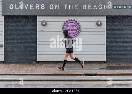 Southend on Sea, Essex, Royaume-Uni. 7 février 2021. La tempête Darcy a atteint Southend on Sea plus tard que prévu, la zone restant humide pendant la nuit. De la neige et des averses de neige sont arrivées vers 7h du matin, ce qui n'a pas dissuadé les joggeurs. Une femme passe devant Oliver's au kiosque du restaurant Beach. Propriété de membres de la famille de Jamie Oliver. Les avertissements de verrouillage COVID 19 restent en place Banque D'Images