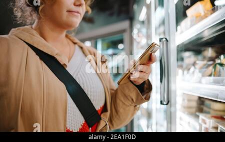 Client qui regarde la liste des courses sur son téléphone mobile. Femme utilisant un téléphone mobile pendant ses achats dans un supermarché. Banque D'Images
