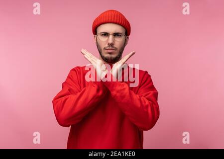 Photo d'un homme attrayant avec une barbe en lunettes et des vêtements rouges. Homme a croisé les mains et montre pas permis, isolé sur fond rose Banque D'Images