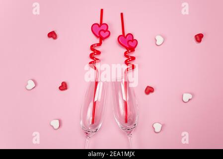Deux verres à champagne avec pailles à boire en plastique rouge et coeurs sur fond rose. Banque D'Images
