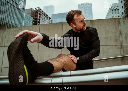 Beau athlète de race blanche qui s'étire les jambes en ville pour l'entraînement physique Banque D'Images