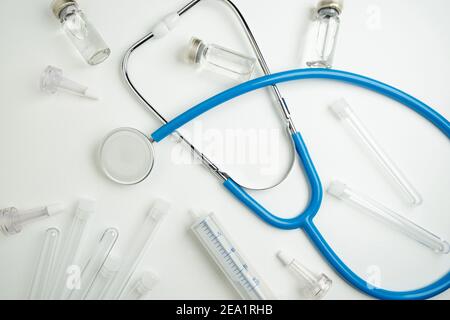 Mise en page médicale sur fond blanc, sur fond plat. Stéthoscope ou phonendoscope bleu entouré de flacons, d'ampoules et de tubes à essai. Banque D'Images