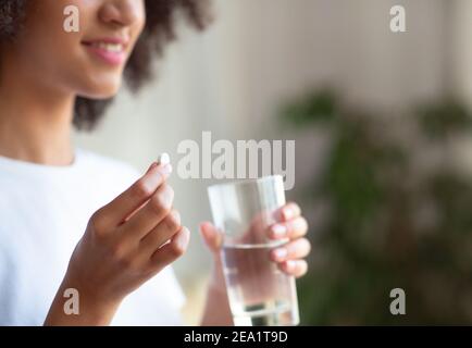 Femme souriante prenant la pilule blanche ronde, tenant le verre d'eau à la main Banque D'Images