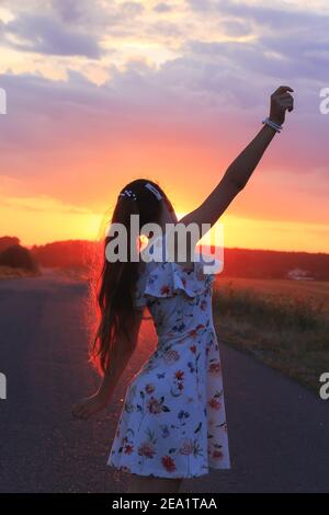 Cute Girl danse sur la route au coucher du soleil. Belle jeune fille avec de longs cheveux souriants. Joyeux enfant. Tons chauds Banque D'Images