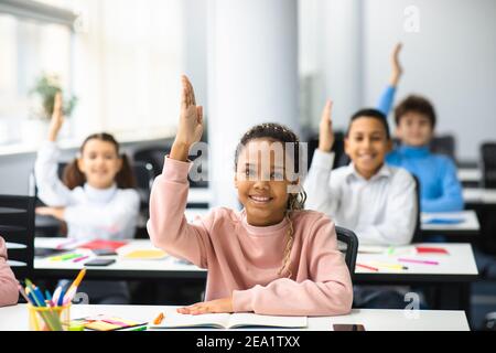 Divers petits écoliers levant les mains en classe Banque D'Images