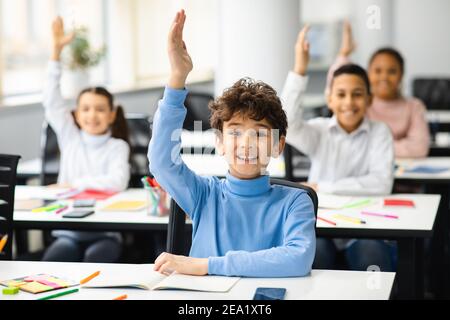 Divers petits écoliers levant les mains en classe Banque D'Images