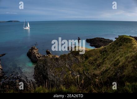 Homme regardant sur la mer turquoise et bleu calme des falaises rocheuses à un yacht blanc de voile comme si dans l'espoir et la contemplation Banque D'Images