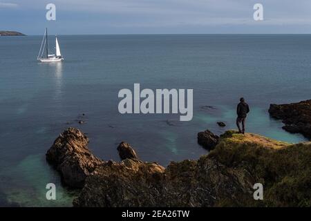 Homme regardant sur la mer turquoise et bleu calme des falaises rocheuses à un yacht blanc de voile comme si dans l'espoir et la contemplation Banque D'Images