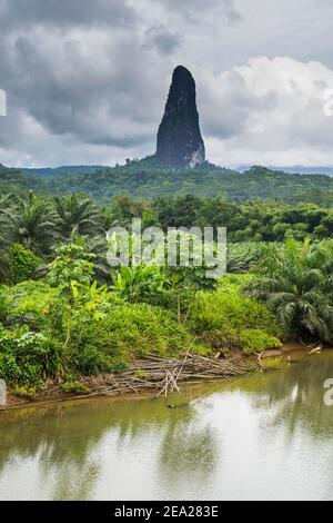 Rivière qui coule avant le monolithe d'anusal, Pico Cao Grande, côte est de Sao Tomé, Sao Tomé-et-principe, océan Atlantique Banque D'Images